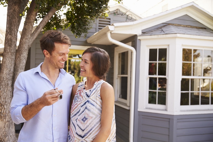 A couple stands outside of their new house with the keys