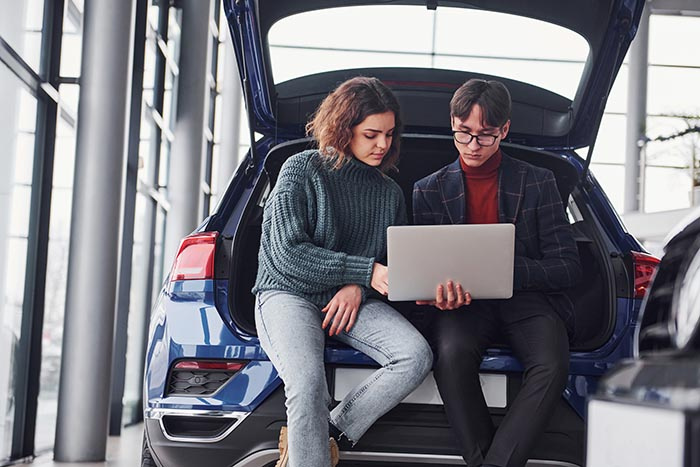 Two Young Professionals Sitting in the Hatchback of a Car with a Laptop