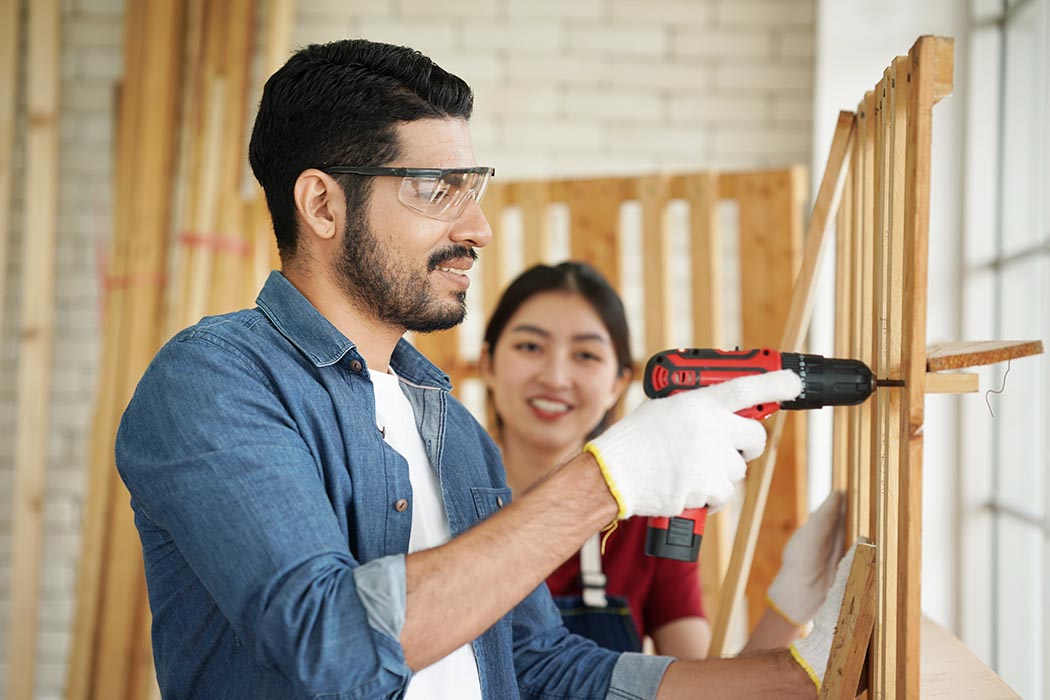 Person using a drill while another person observes